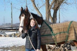 Caleigh Copelin poses with a brown horse covered in a winter blanket.